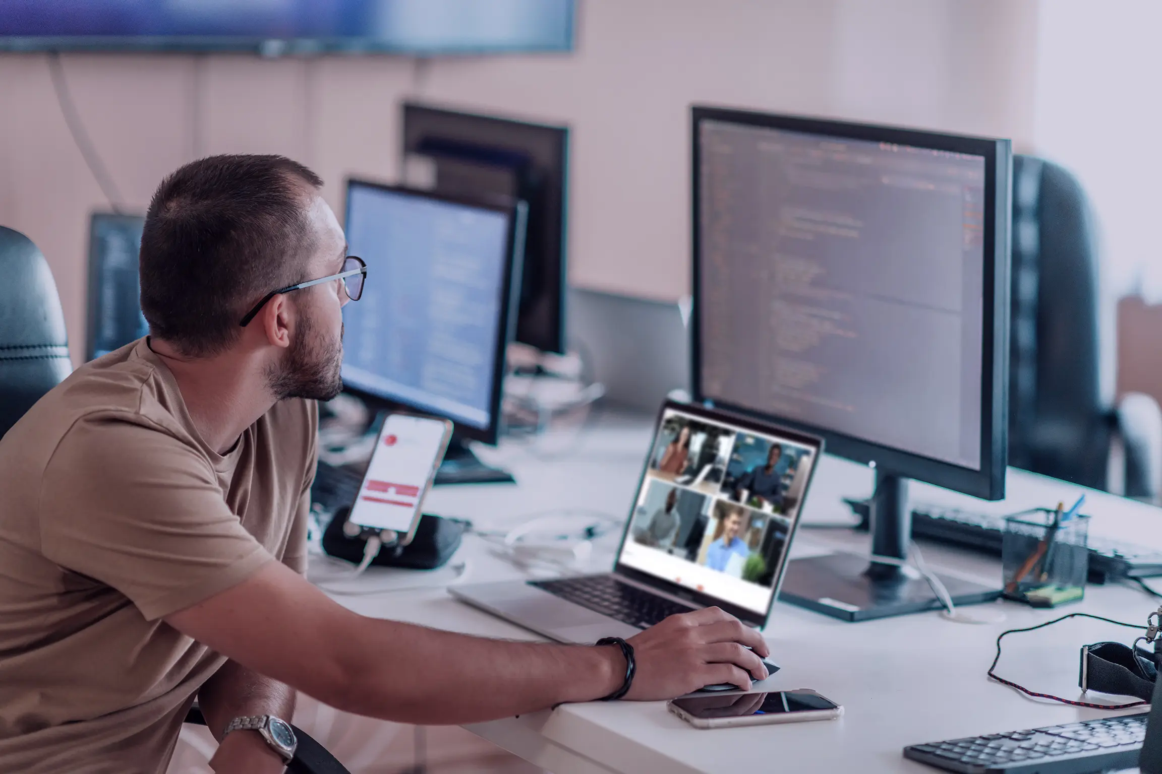 A product team member concentrating on multiple monitors, one with code, and the other displaying a video conference with team members.